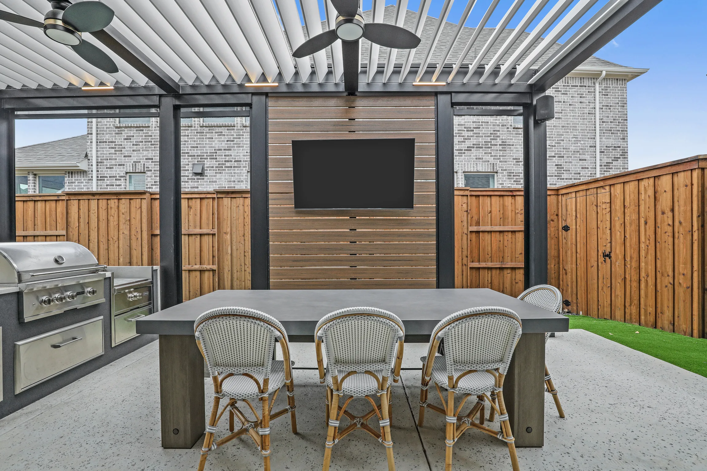 black-white-louvered-pergola-with-tv-on-the-wall-and-outdoor-living-furniture-and-kitchen-with-wooden-fence-in-omaha-ne