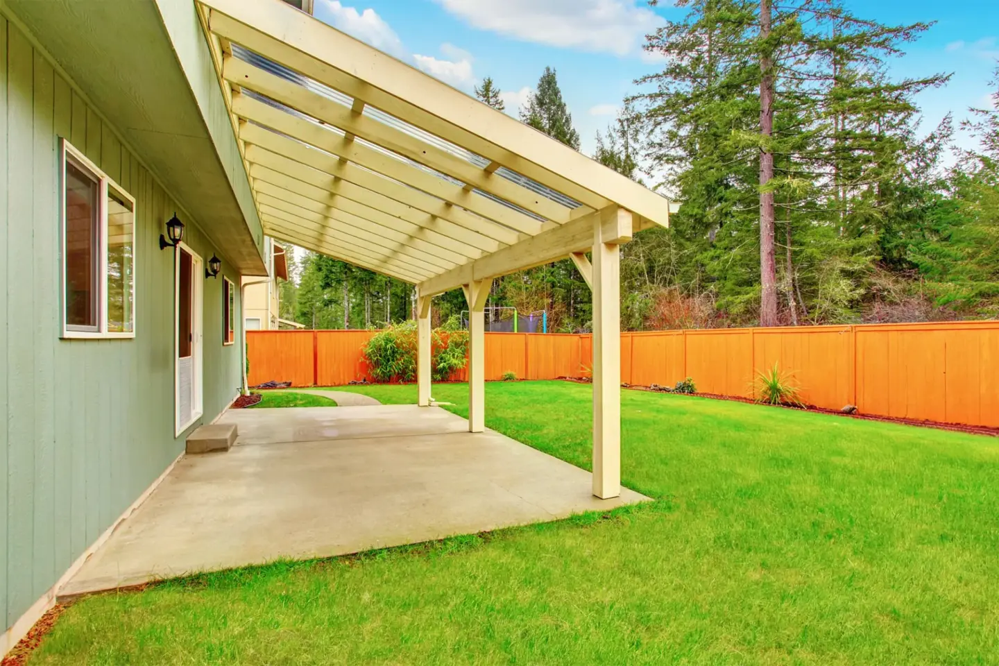 covered-backyard-porch-with-concrete-floor-and-wooden-fence-with-big-trees-on-the-background-in-omaha-ne